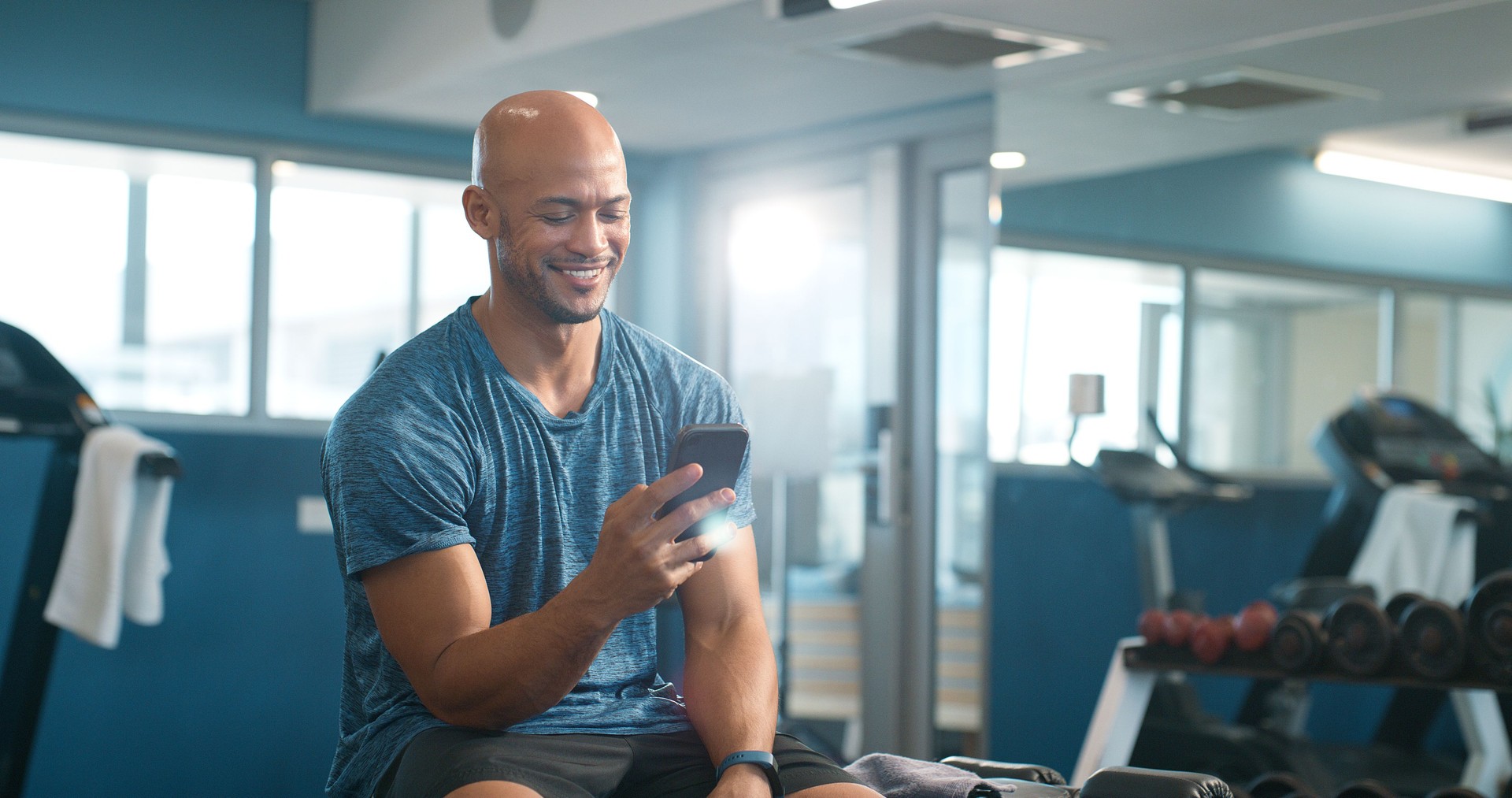 Fitness, happy and phone with man in gym for break from exercise, health or training routine. App, social media and text message with smile of athlete person tracking progress of workout on mobile